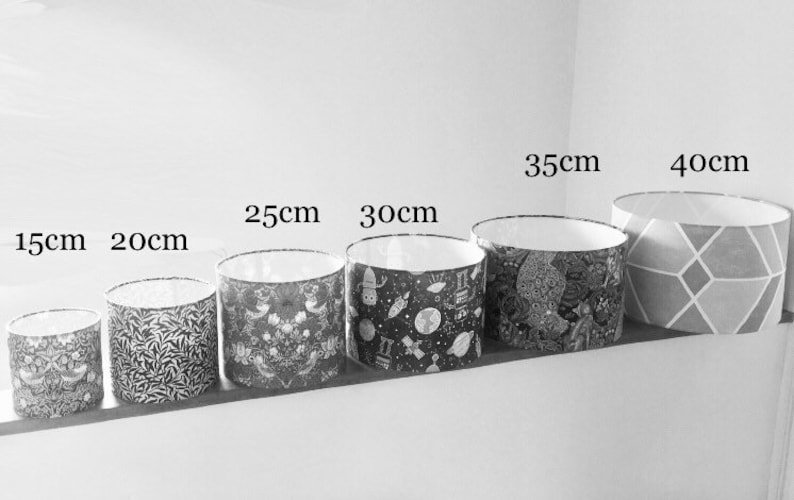 Op de afbeelding: Zeven lampenkappen in verschillende maten met verschillende patronen. De lampenkappen zijn van klein naar groot opgesteld, met de afmetingen 15 cm, 20 cm, 25 cm, 30 cm, 35 cm en 40 cm die boven elke kap zijn aangegeven.