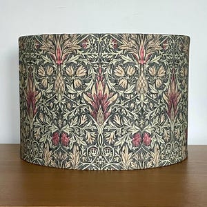 May include: A drum lampshade with a repeating floral design in burgundy, cream, and olive green. The pattern features stylized flowers and leaves on a dark background. The lampshade is suitable for a table or floor lamp and has a diameter of approximately 30 cm.