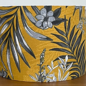 May include: A yellow lampshade with a tropical print featuring black and grey palm leaves and flowers.