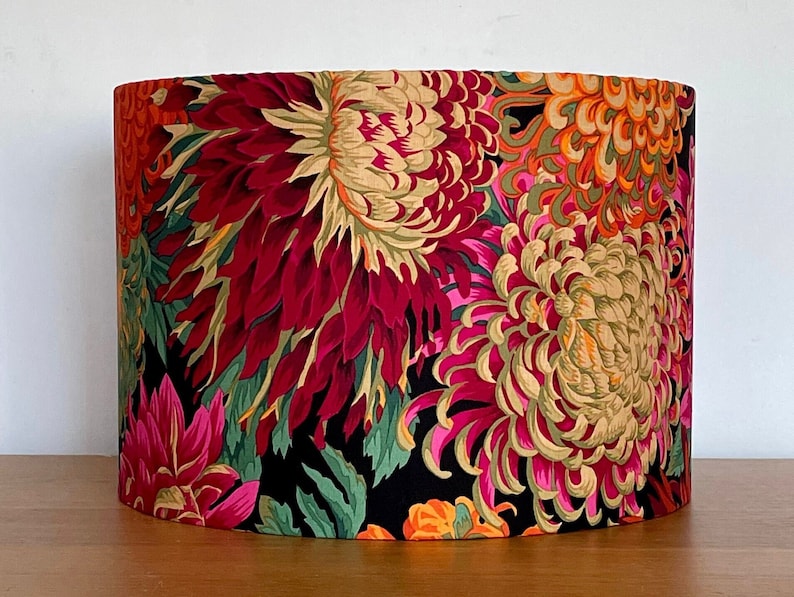 Op de afbeelding: Een zwarte lampenkap met een bloemenpatroon met grote roze, rode en gele bloemen op een zwarte achtergrond.