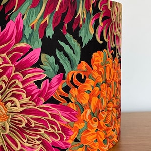 Op de afbeelding: Een zwarte lampenkap met een bloemenpatroon met roze, oranje en groene chrysanten.