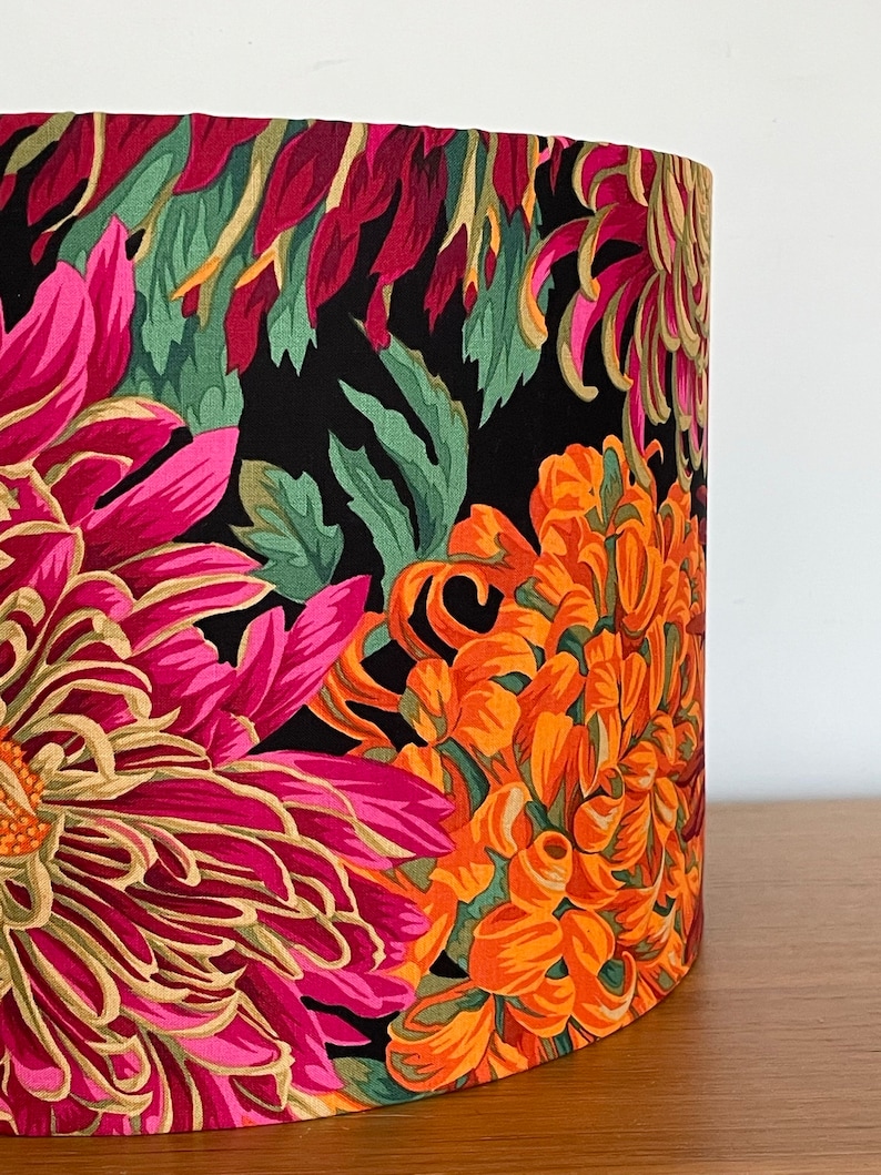 Op de afbeelding: Een zwarte lampenkap met een bloemenpatroon met roze, oranje en groene chrysanten.