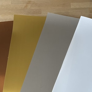Op de afbeelding: Vier vellen papier in verschillende kleuren: bruin, goud, grijs en wit.