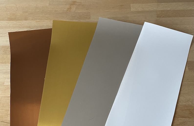 Op de afbeelding: Vier vellen papier in verschillende kleuren: bruin, goud, grijs en wit.