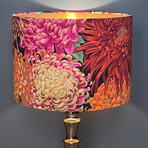 Op de afbeelding: Een gouden tafellamp met een zwart-witte bloemenlampkap met roze, oranje en rode chrysanten.