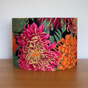 Op de afbeelding: Een zwarte lampenkap met een bloemenprint met roze, oranje en groene chrysanten.