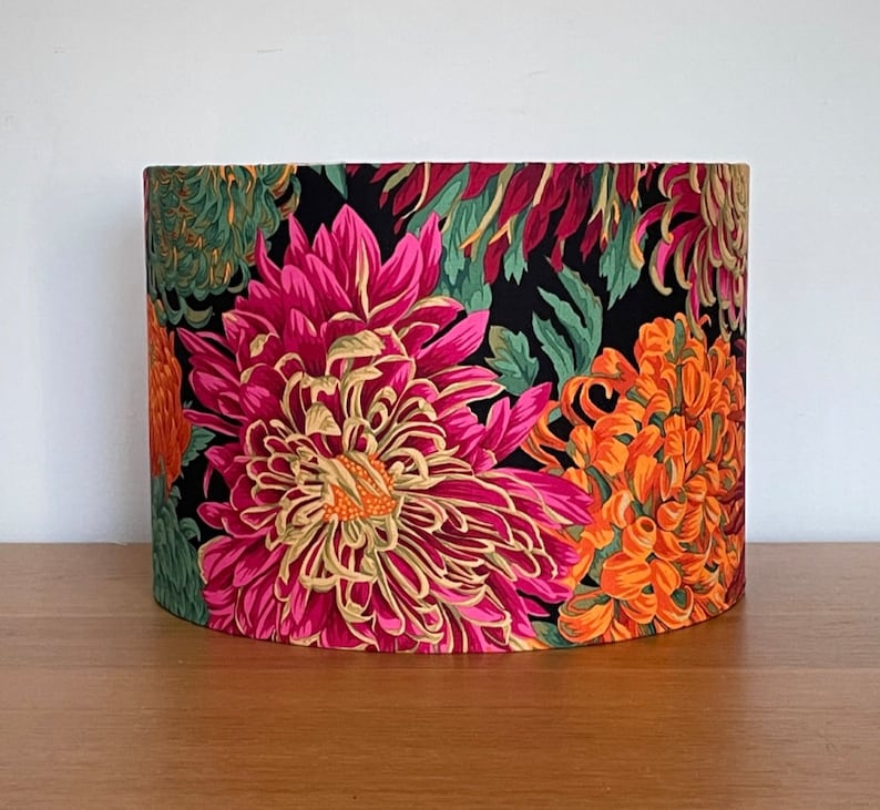 Op de afbeelding: Een zwarte lampenkap met een bloemenprint met roze, oranje en groene chrysanten.