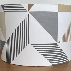 May include: A white lampshade with a geometric pattern in shades of grey, brown, and beige. The pattern features stripes and triangles.