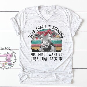 May include: A white t-shirt with a vintage-style graphic of a cow wearing a red bandana. The text "Your crazy is showing you might want to tuck that back in" is printed on the shirt.