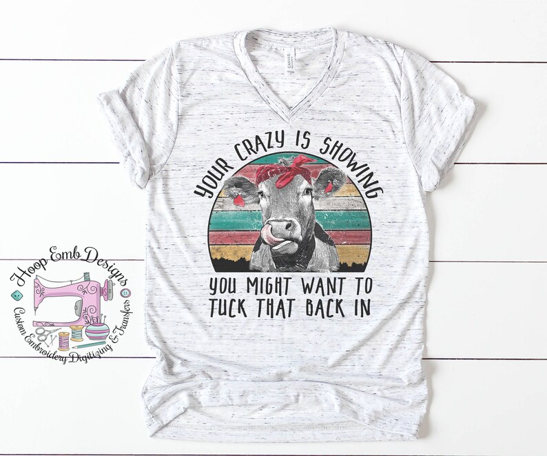 May include: A white t-shirt with a vintage-style graphic of a cow wearing a red bandana. The text "Your crazy is showing you might want to tuck that back in" is printed on the shirt.