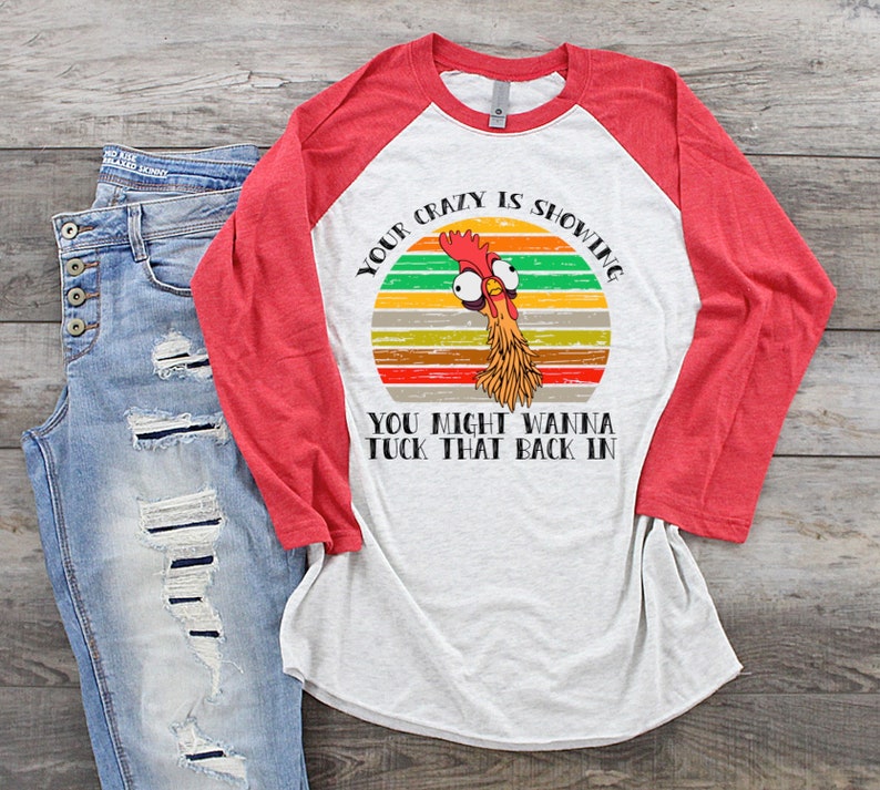 May include: A white and red baseball tee shirt with a retro-style graphic of a chicken with the text "Your crazy is showing. You might wanna tuck that back in."