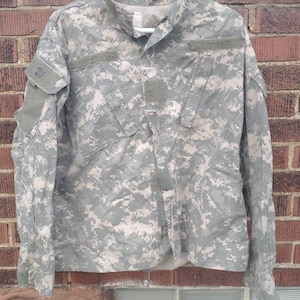 May include: A green, brown, and tan camouflage military jacket with long sleeves and a button-up front.