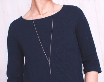 Pode incluir: Um vestido azul marinho texturizado com mangas três quartos e decote redondo. Um colar de prata com um pingente de barra pende na frente do vestido. O vestido é feito de tecido texturizado.