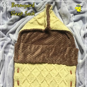 May include: A yellow knitted baby sleep sack with a brown fleece lining and a hood. The sleep sack has buttons down the side and the text "Bromyard Sleep Sack" at the top. The text "Dizzy Tyke Designs" is at the bottom.