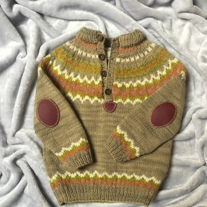 Puede incluir: Un suéter de punto marrón con un patrón geométrico colorido, con parches de cuero en los codos y un cierre de botón en el cuello.