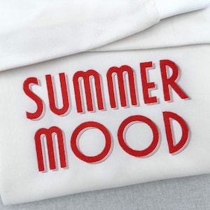 May include: A white sweatshirt with the words "SUMMER MOOD" embroidered in red. The sweatshirt has a folded collar and a soft, casual appearance, perfect for warm weather.