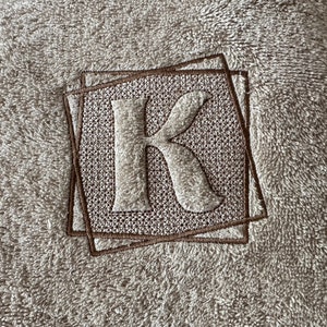 May include: A brown plush towel with a brown embroidered letter K in the center.
