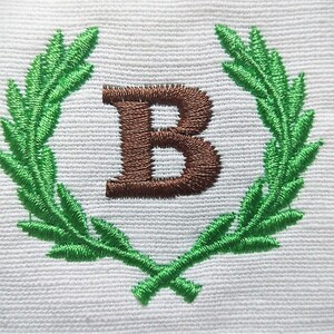 以下が含まれることがあります： 緑色の刺繍された月桂樹の輪の中に、茶色の「B」の文字が刺繍されています。