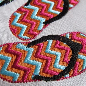 May include: Close-up of two embroidered flip-flop designs. The flip-flops are orange, pink, and blue with a black outline. The designs are stitched in a chevron pattern.