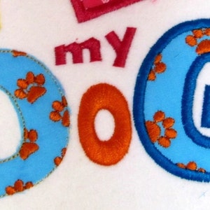 May include: Blue felt letters spelling "I love my dog" with orange paw print designs. The letters are outlined in blue and orange.