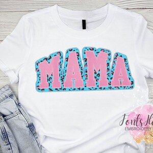 May include: White t-shirt with a pink and blue "MAMA" design featuring a leopard print pattern.