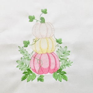 May include: A stack of three embroidered pumpkins in pink, yellow, and white with green leaves. The pumpkins are stacked on top of each other and have a vine running up the side.