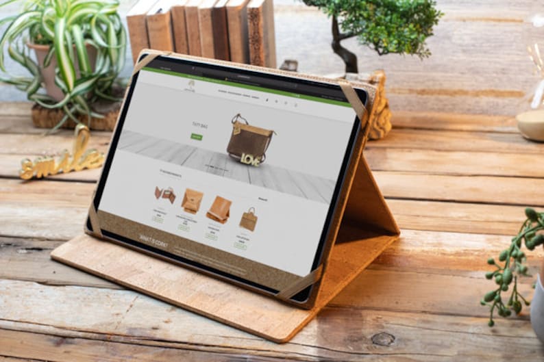May include: A brown leather tablet case with a stand, displaying a website on a tablet screen. The website features a variety of leather bags and purses, including a brown crossbody bag with a gold "LOVE" charm.