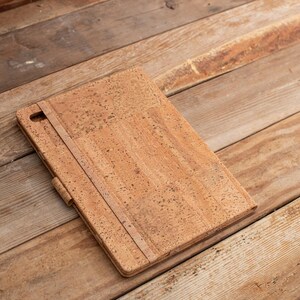 Puede incluir: Una funda rectangular para tableta hecha de material de corcho natural con una textura moteada en tonos bronceado y marr&oacute;n. La funda cuenta con una correa el&aacute;stica vertical en la cubierta frontal y una peque&ntilde;a abertura en la esquina.