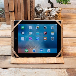 Puede incluir: Una tableta asegurada en una funda protectora de color marr&oacute;n claro con textura de corcho y correas el&aacute;sticas en las esquinas. La pantalla muestra una cuadr&iacute;cula est&aacute;ndar de iconos de aplicaciones, incluyendo mensajes, calendario, fotos, c&aacute;mara y ajustes.