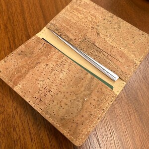 May include: A brown cork wallet with a stitched edge. The wallet is open to reveal multiple card slots and a cash pocket.