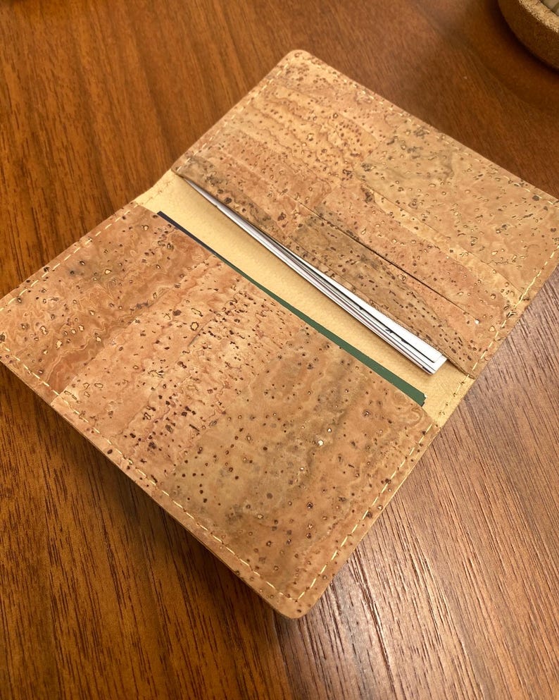 May include: A brown cork wallet with a stitched edge. The wallet is open to reveal multiple card slots and a cash pocket.