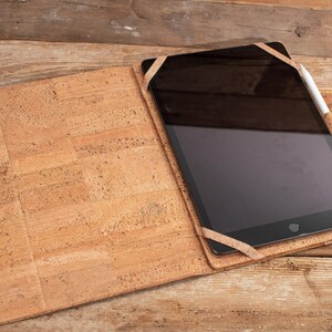 May include: A cork tablet case with a brown leather strap and a black tablet with a white stylus.
