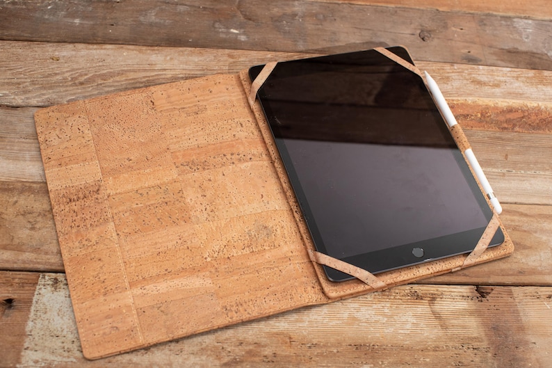May include: A cork tablet case with a brown leather strap and a black tablet with a white stylus.