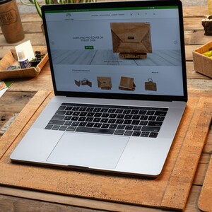 May include: A laptop on a cork desk mat, with a matching mouse mat and a coffee cup. The laptop screen shows a website selling cork products, including a tablet case. The desk is made of wood.