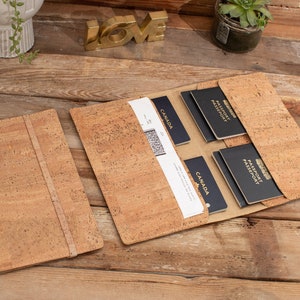 May include: A cork travel wallet with two passport holders and a slot for boarding passes. The wallet is open and the passport holders are visible. The wallet is made of natural cork and has a brown colour.