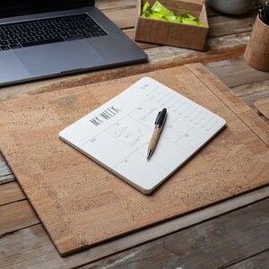 May include: A cork desk setup with a laptop, pen holder, mouse, and desk pad. A white notepad with the words "MY WEEK" and a pen with a cork barrel are on the desk pad. The desk pad and mouse pad are made of cork.