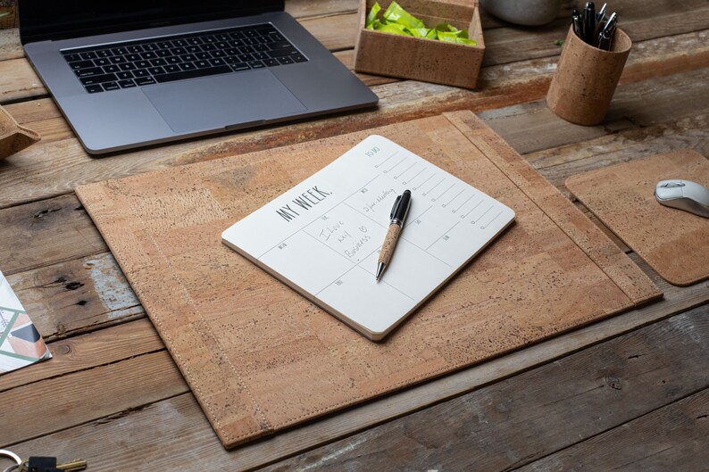 May include: A cork desk setup with a laptop, pen holder, mouse, and desk pad. A white notepad with the words "MY WEEK" and a pen with a cork barrel are on the desk pad. The desk pad and mouse pad are made of cork.