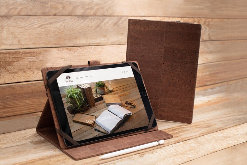 May include: A brown leather iPad case with a cork exterior. The case is open and an iPad is inside. The iPad screen shows a website with the text "A choice for every story".