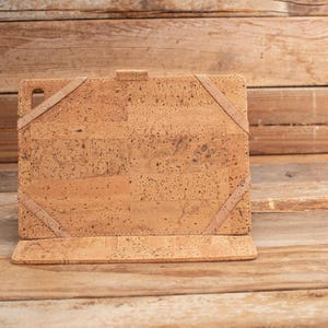 Puede incluir: Una funda rectangular para tableta hecha de material de corcho marr&oacute;n claro con una textura moteada. La funda cuenta con cuatro correas el&aacute;sticas en las esquinas para asegurar un dispositivo y un peque&ntilde;o recorte en la esquina superior izquierda.