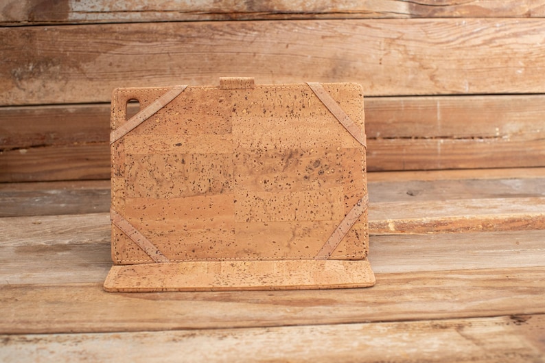 Puede incluir: Una funda rectangular para tableta hecha de material de corcho marr&oacute;n claro con una textura moteada. La funda cuenta con cuatro correas el&aacute;sticas en las esquinas para asegurar un dispositivo y un peque&ntilde;o recorte en la esquina superior izquierda.