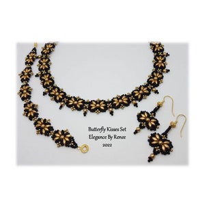 May include: A black and gold beaded necklace and bracelet set with matching earrings. The jewellery features a flower design and is labelled "Butterfly Kisses Set Elegance By Renee 2022".