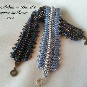May include: Two beaded bracelets, one blue and silver, the other blue, brown, and purple. The bracelets are called "Bead-A-Saurus Bracelet Elegance by Renee 2014".