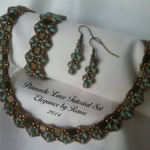 Op de afbeelding: Een set teal en gouden kralen sieraden, waaronder een ketting en oorbellen. De ketting is een delicaat, ingewikkeld ontwerp met een gegolfde rand. De oorbellen zijn eenvoudig en elegant, met een druppelvorm. De sieraden zijn gelabeld "Pinnacle Lace Tutorial Set Elegance by Renee 2014".