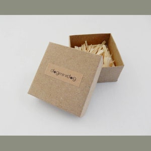 May include: A small, brown cardboard box with the text "dogminidog" on the side. The box is open and filled with wood shavings.