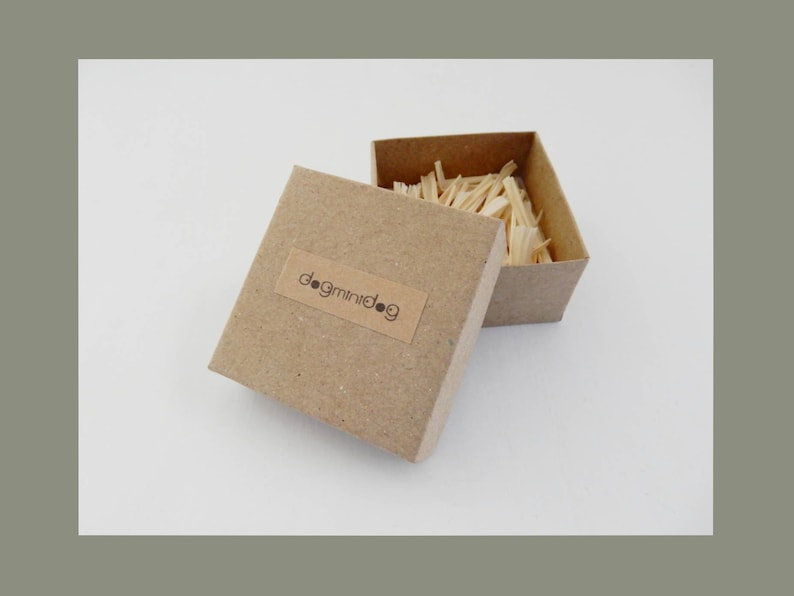 May include: A small, brown cardboard box with the text "dogminidog" on the side. The box is open and filled with wood shavings.