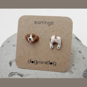 Pode incluir: Um par de brincos com a cabeça de um cão castanho e branco de um lado e a parte traseira do cão do outro. Os brincos estão em um cartão castanho com o texto "earrings" e "dogminidog".