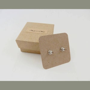 May include: A pair of silver stud earrings on a brown card with the text "dogminidog" on a brown box.