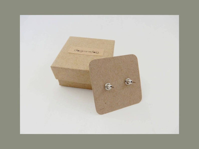 May include: A pair of silver stud earrings on a brown card with the text "dogminidog" on a brown box.