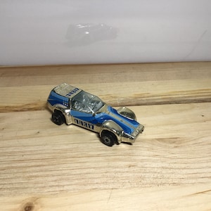 May include: A vintage toy car in gold and blue. The car has a streamlined design with a blue stripe down the center and the word "DARE" printed on the side. The car has black wheels and a clear windshield.