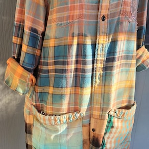 May include: A long-sleeved, orange, blue, and green plaid shirt with a faded, distressed look. The shirt has multiple pockets and a button-up front.